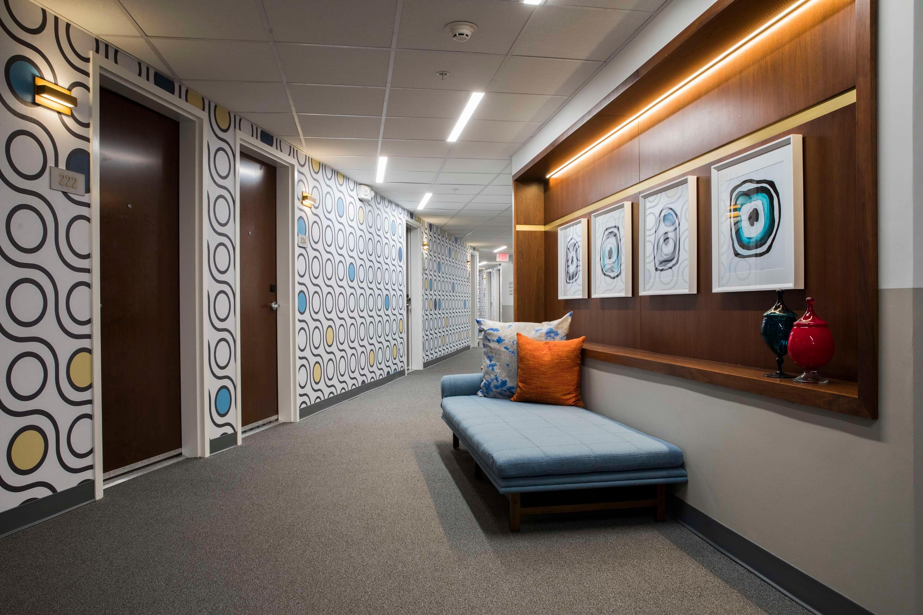 A hallway with patterned walls, a bench with pillows, and framed artwork on the wall.