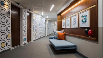 A hallway with patterned walls, a bench with pillows, and framed artwork on the wall.