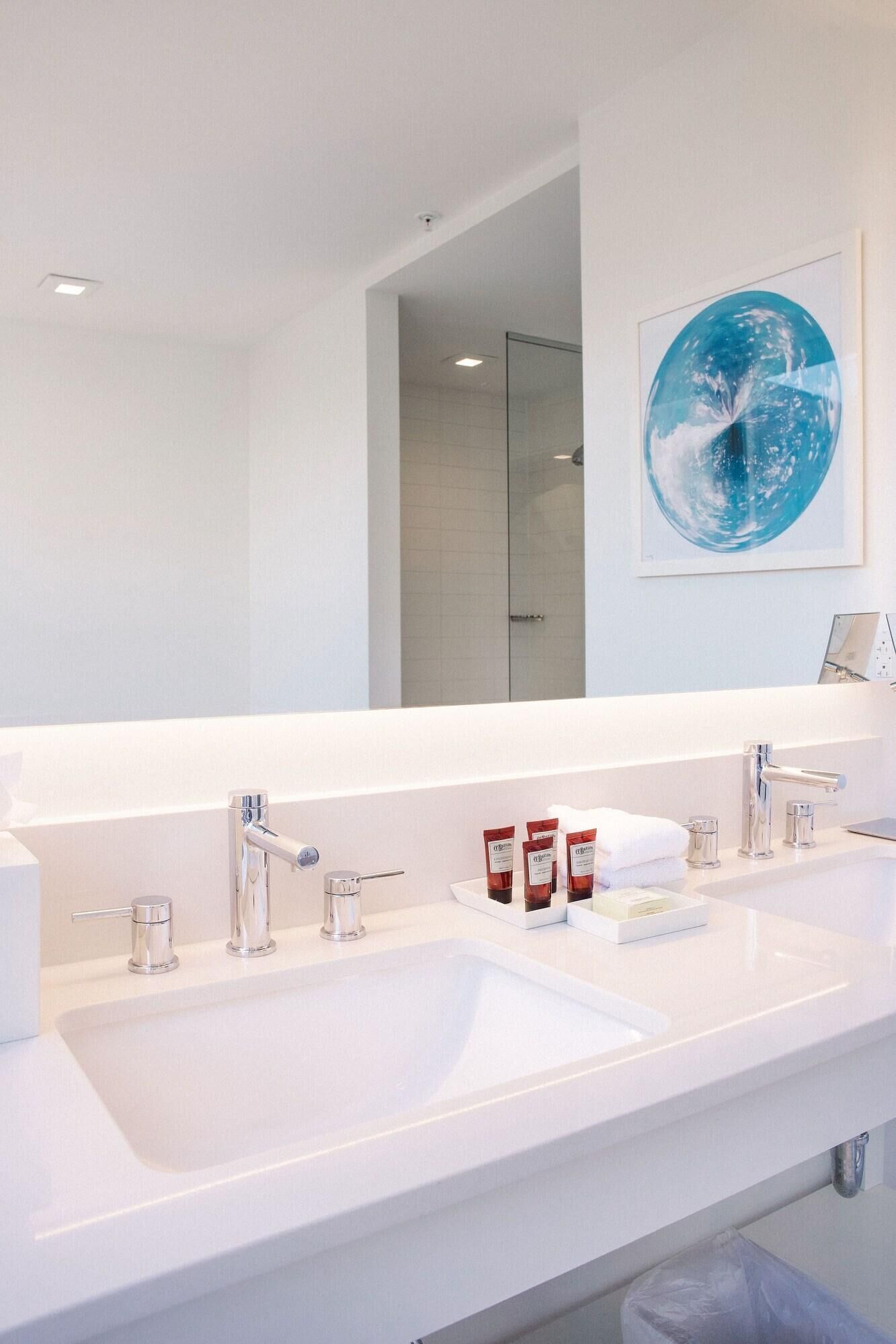 A modern bathroom with a large mirror, two sinks, and a glass shower enclosure.