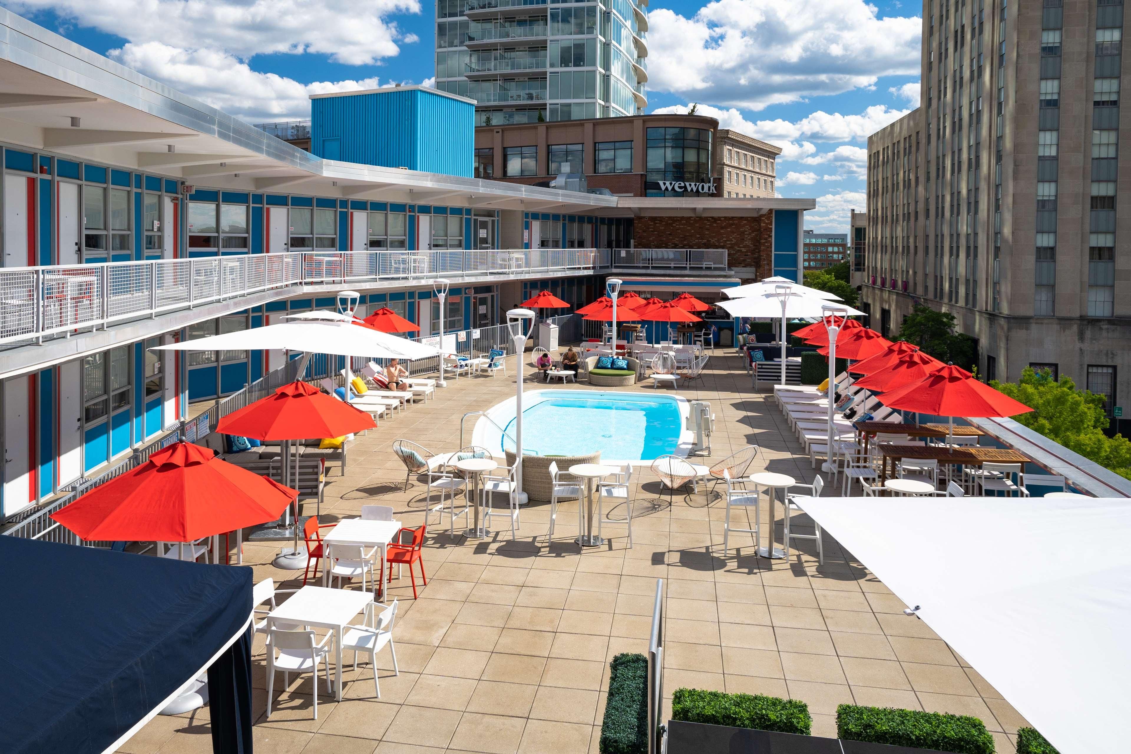 A rooftop pool area with multiple red umbrellas, lounge chairs, and a swimming pool.