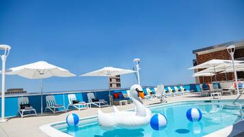 A swimming pool with a swan float, lounge chairs, umbrellas, and a view of the ocean.