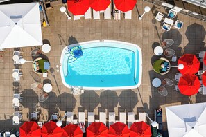 Vista aérea de una piscina rodeada de sillas de descanso y sombrillas.