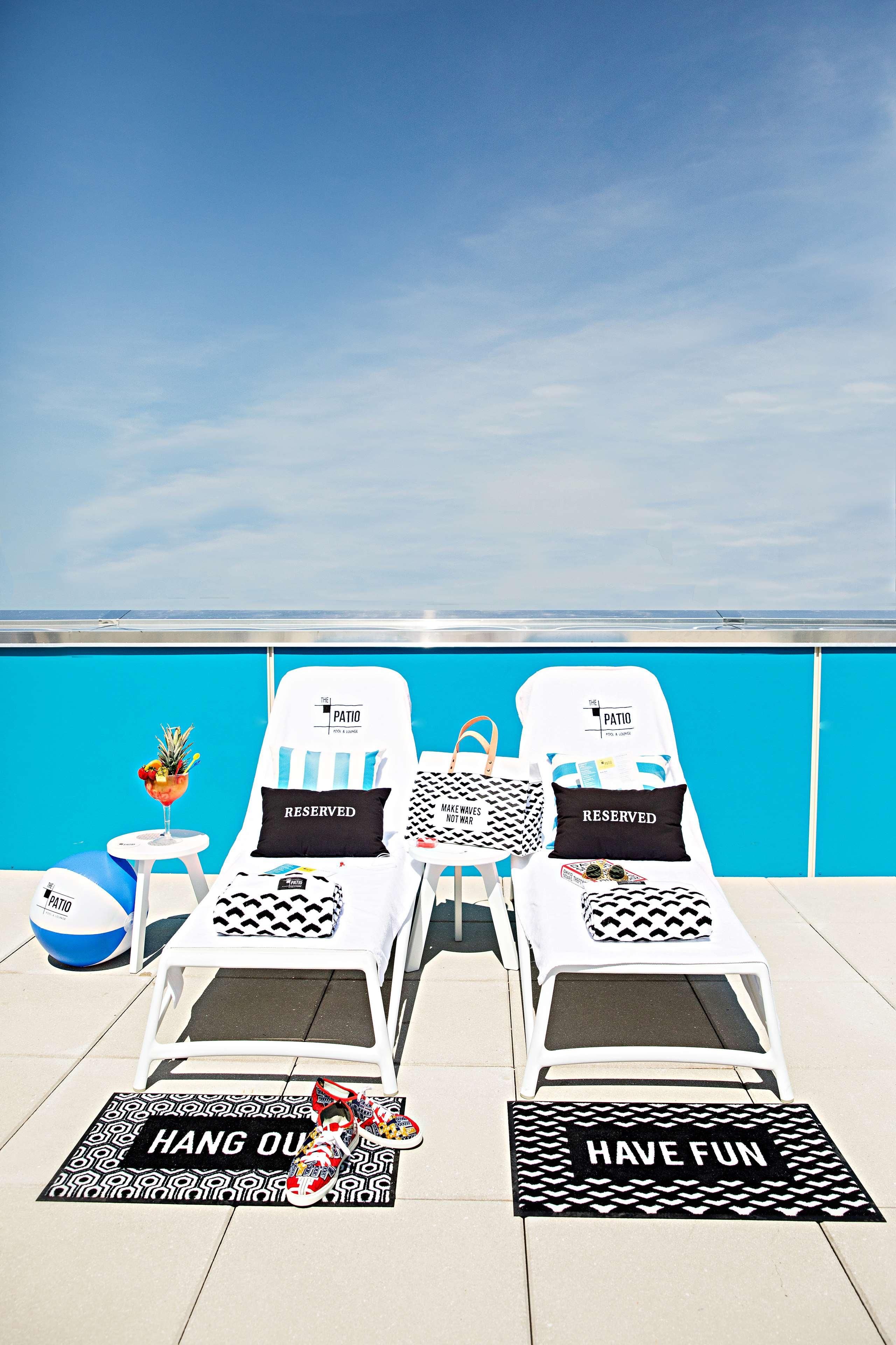 A poolside area with two lounge chairs, a beach ball, a drink, and a towel with 'HAVE FUN' text.