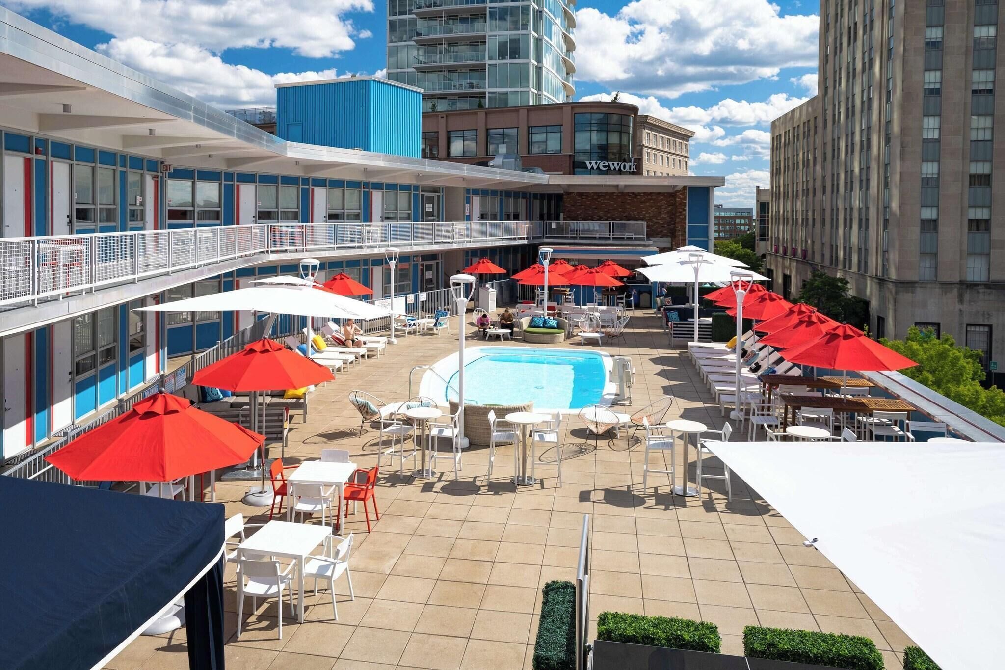 A rooftop pool area with red umbrellas, lounge chairs, and a swimming pool.