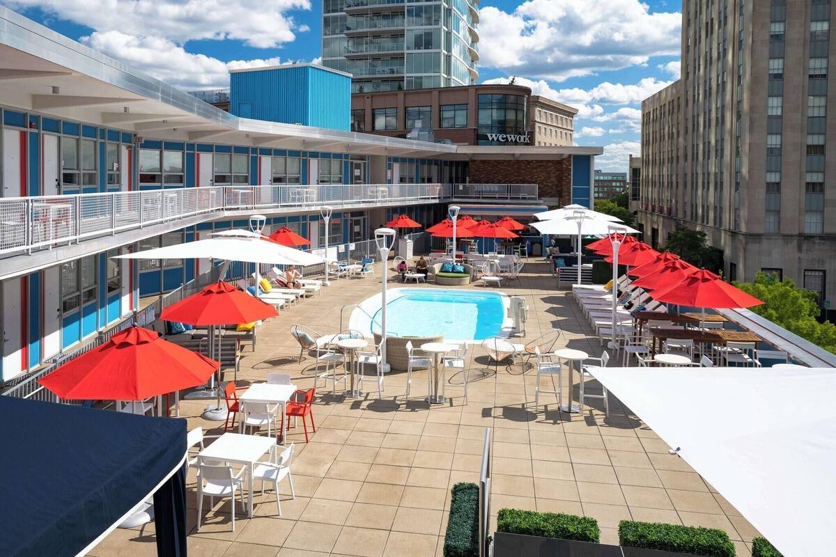 A rooftop pool area with red umbrellas, lounge chairs, and a swimming pool.