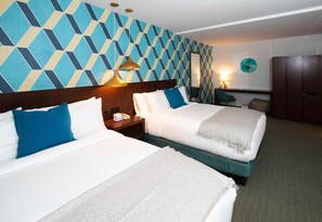 Habitación de hotel con dos camas, un gran muro con estampado geométrico, un espejo, un escritorio con lámpara y un armario.