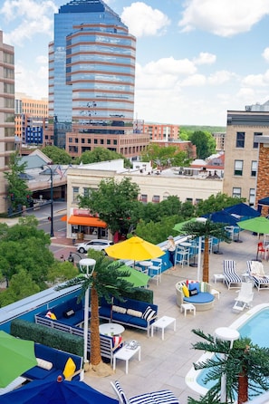 A rooftop pool area with lounge chairs, umbrellas, and a view of surrounding buildings. - Unscripted Durham (Durham)