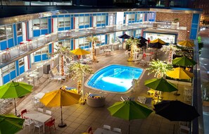 An indoor pool area with multiple lounge chairs and umbrellas, surrounded by a multi-level building with balconies. - Unscripted Durham (Durham)