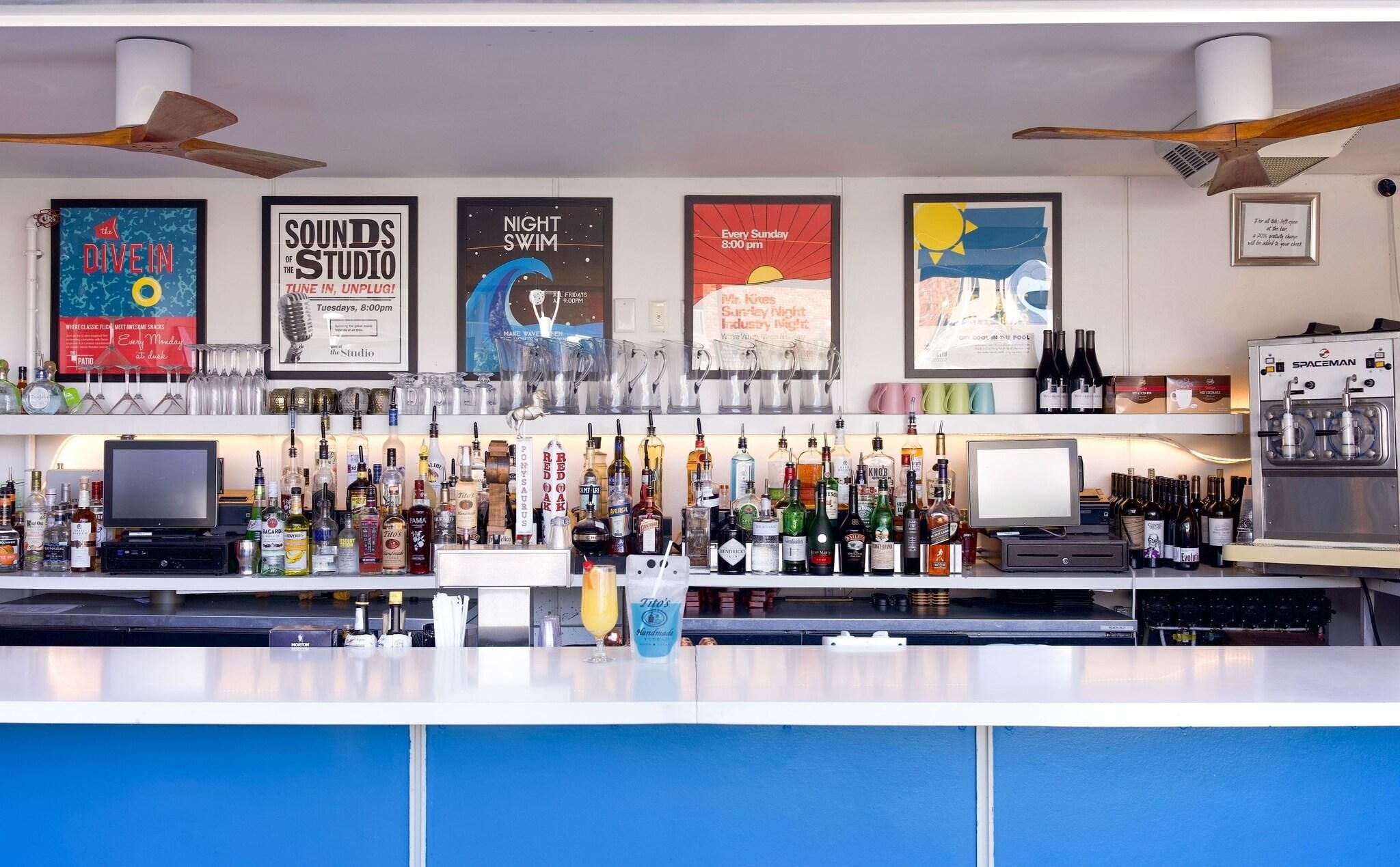 A bar area with multiple liquor bottles, a Spaceman machine, and posters advertising events like 'The Dive In' and 'Night Swim'.