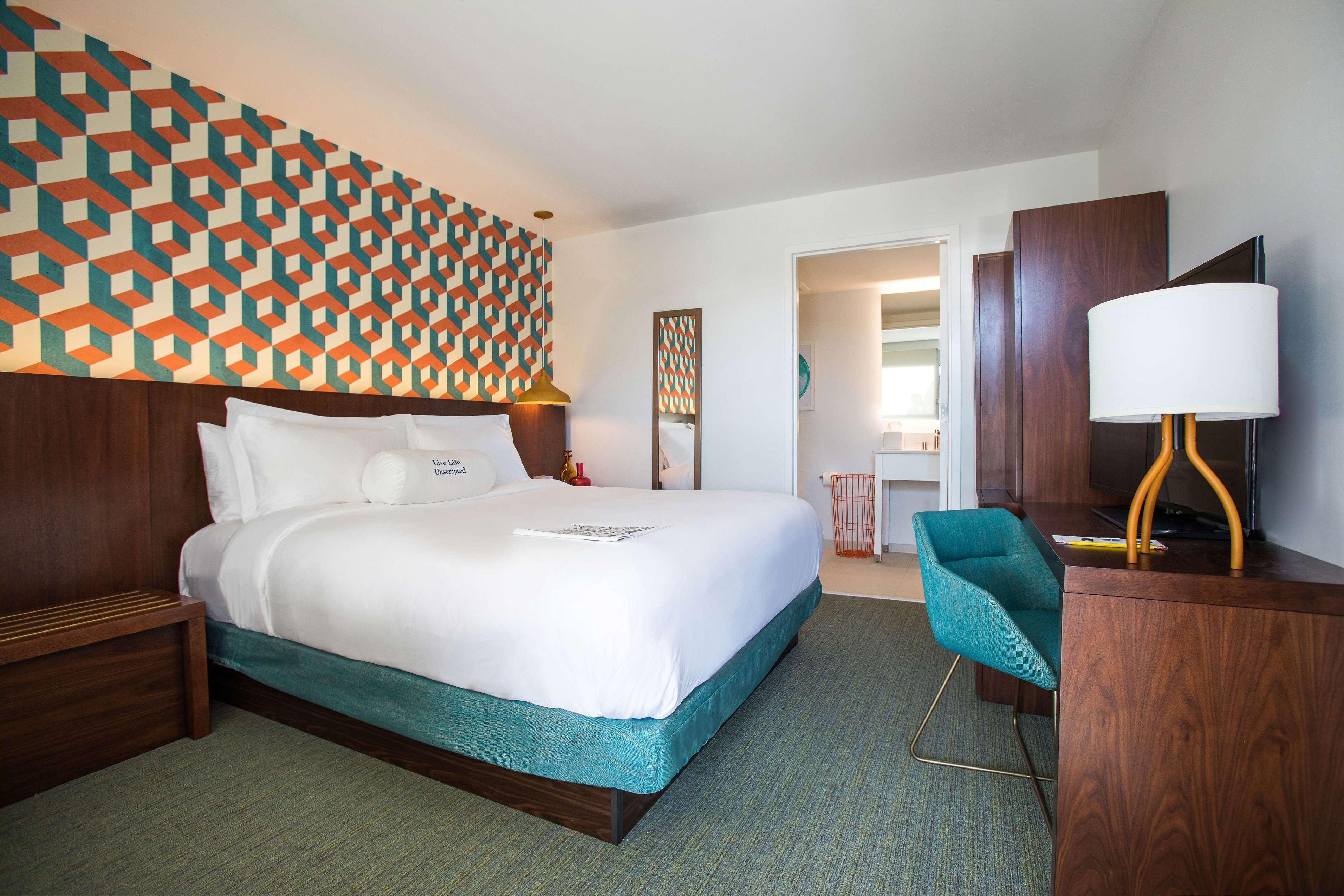 Habitación de hotel con cama, escritorio, silla, lámpara y pared con diseño.