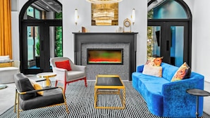 Un salon moderne avec une cheminée, un canapé bleu, un fauteuil noir et un tapis à motifs.
