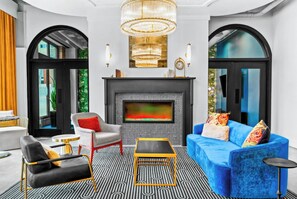 A modern living room with a fireplace, a blue sofa, a black armchair, and a patterned rug. - Hotel Indigo Omaha Downtown (Omaha)