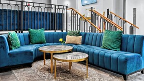 Een moderne hotel lobby met een blauwe modulaire bank, een ronde salontafel en een trap met een houten leuning.