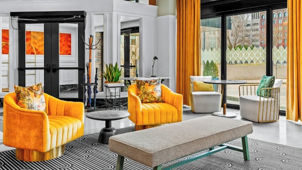 Un hall d'entrée moderne avec deux fauteuils orange éclatants, un banc et une table ronde.