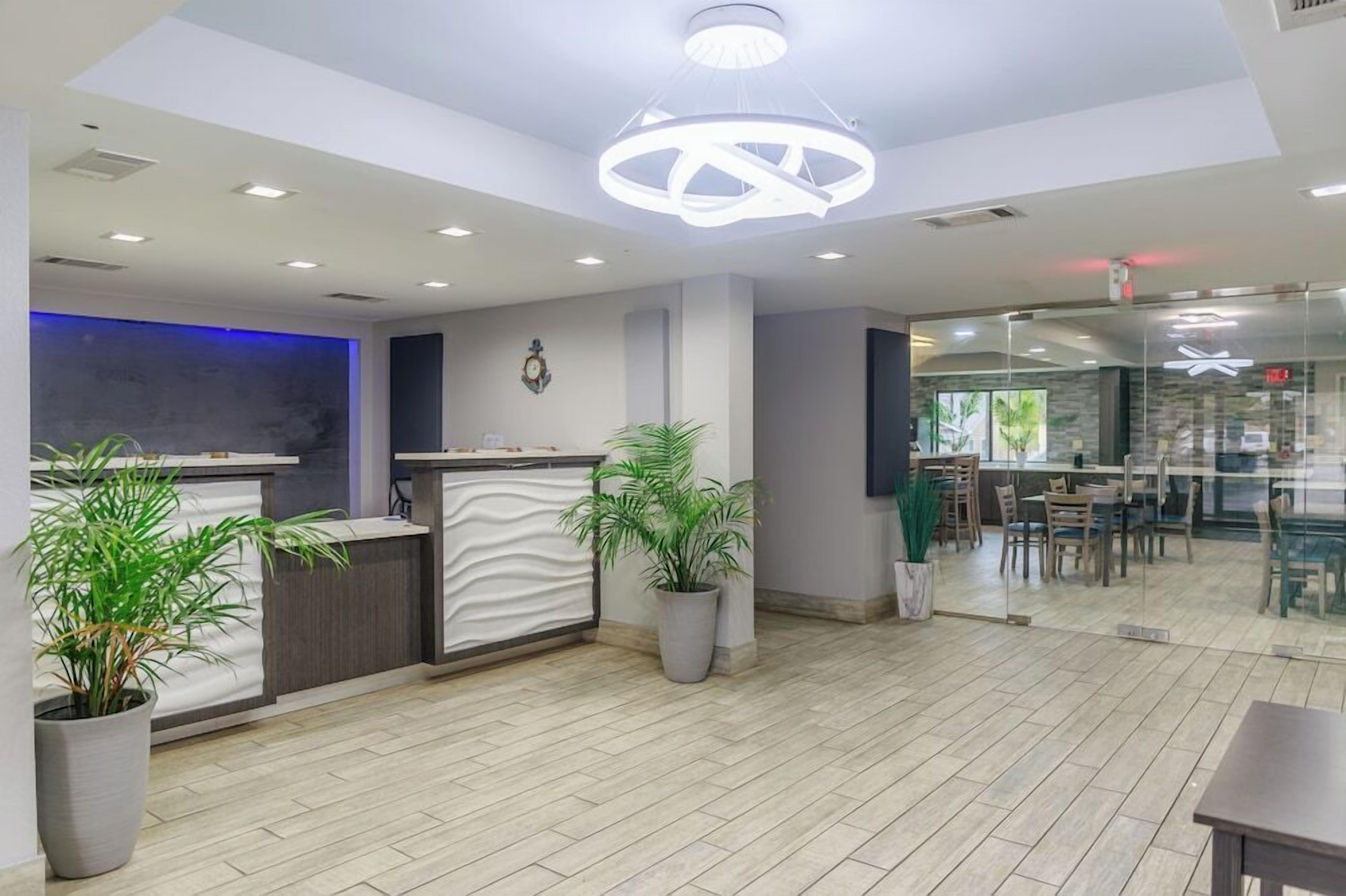 A modern reception area with a reception desk, potted plants, and a dining area with tables and chairs.