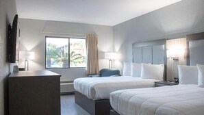 A hotel room with two beds, a desk, a chair, and a large window with curtains. - Howard Johnson Inn Tybee Island Savannah Ga (Tybee Island)