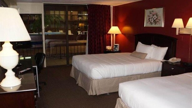 Ein Hotelzimmer mit zwei Betten, einem Schreibtisch mit Lampe, einem Sessel, einer Schreibtischlampe, einem Telefon und einem Fenster mit Vorhängen.
