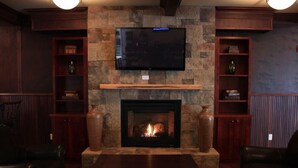A living room with a stone fireplace, a flat-screen TV mounted above it, and leather seating.