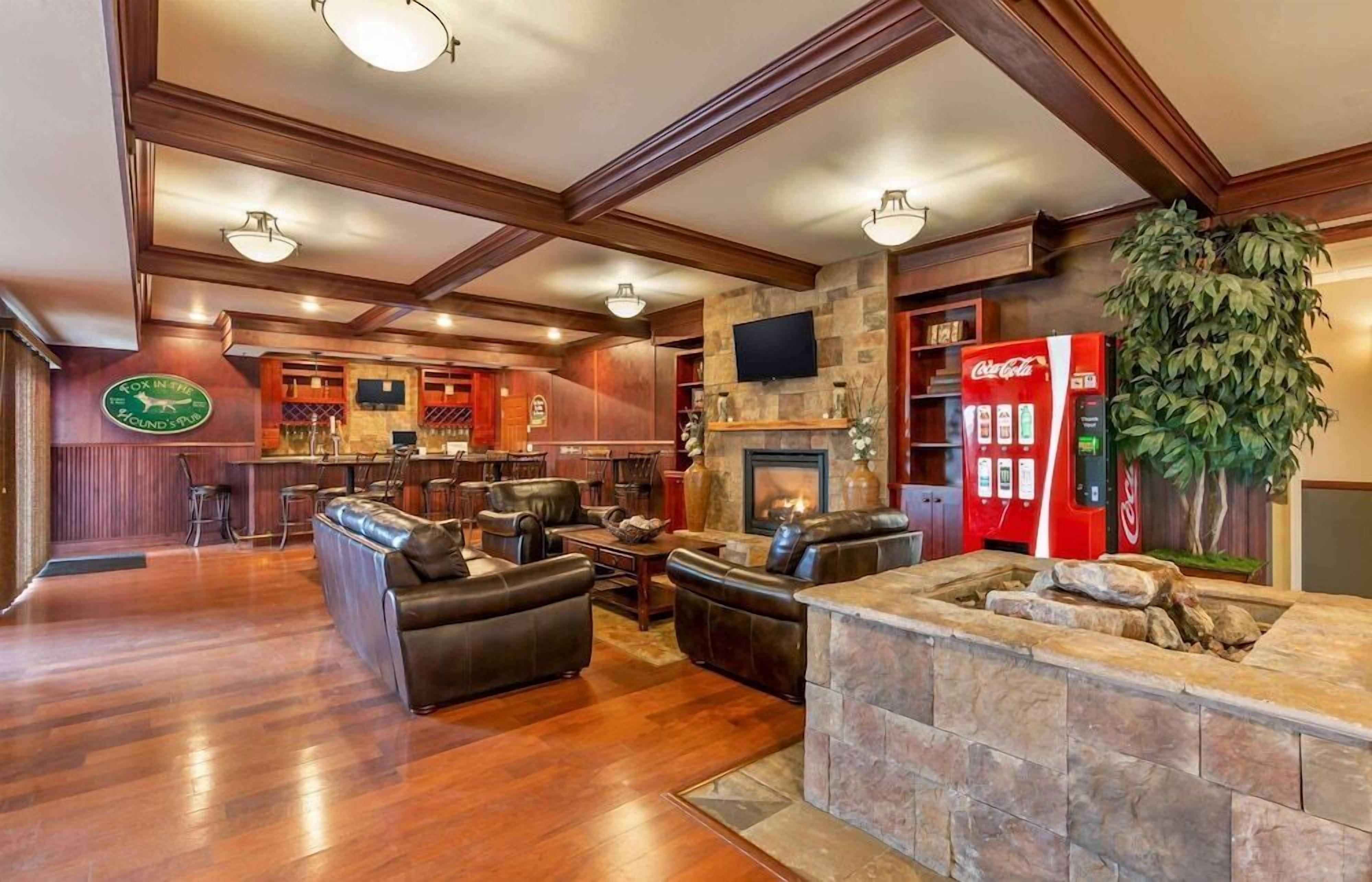A spacious living area with a stone fireplace, leather sofas, a bar area with a red Coca-Cola refrigerator, and a television mounted on the wall.