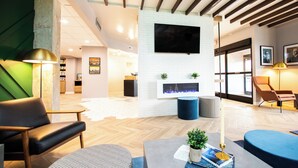 A modern interior with a fireplace, seating area, and a flat-screen TV mounted on the wall. - Hotel Denim (Greensboro)