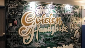 A wall with graffiti and text, including 'The Golden Handshake North Carolina' and 'DENIM'. - Hotel Denim (Greensboro)