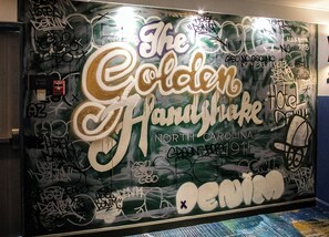 A wall with graffiti and text, including 'The Golden Handshake North Carolina' and 'DENIM'. - Hotel Denim (Greensboro)