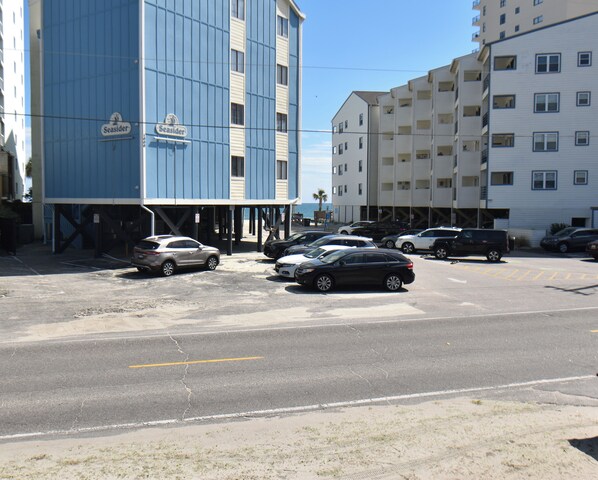 A parking lot with several cars, a blue building with 'Seaside' signage, and a white building with multiple windows. - Sunset Square L - 2nd Row in Garden City Beach (Garden City Beach)