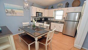 Una cocina con armarios blancos, un refrigerador de acero inoxidable, un microondas y una mesa de comedor con sillas.