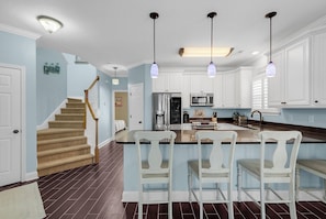 A modern kitchen with white cabinets, a central island with bar stools, stainless steel appliances, and pendant lighting. - Aloha Y'all - 2nd Row in Surfside Beach! (Surfside Beach)