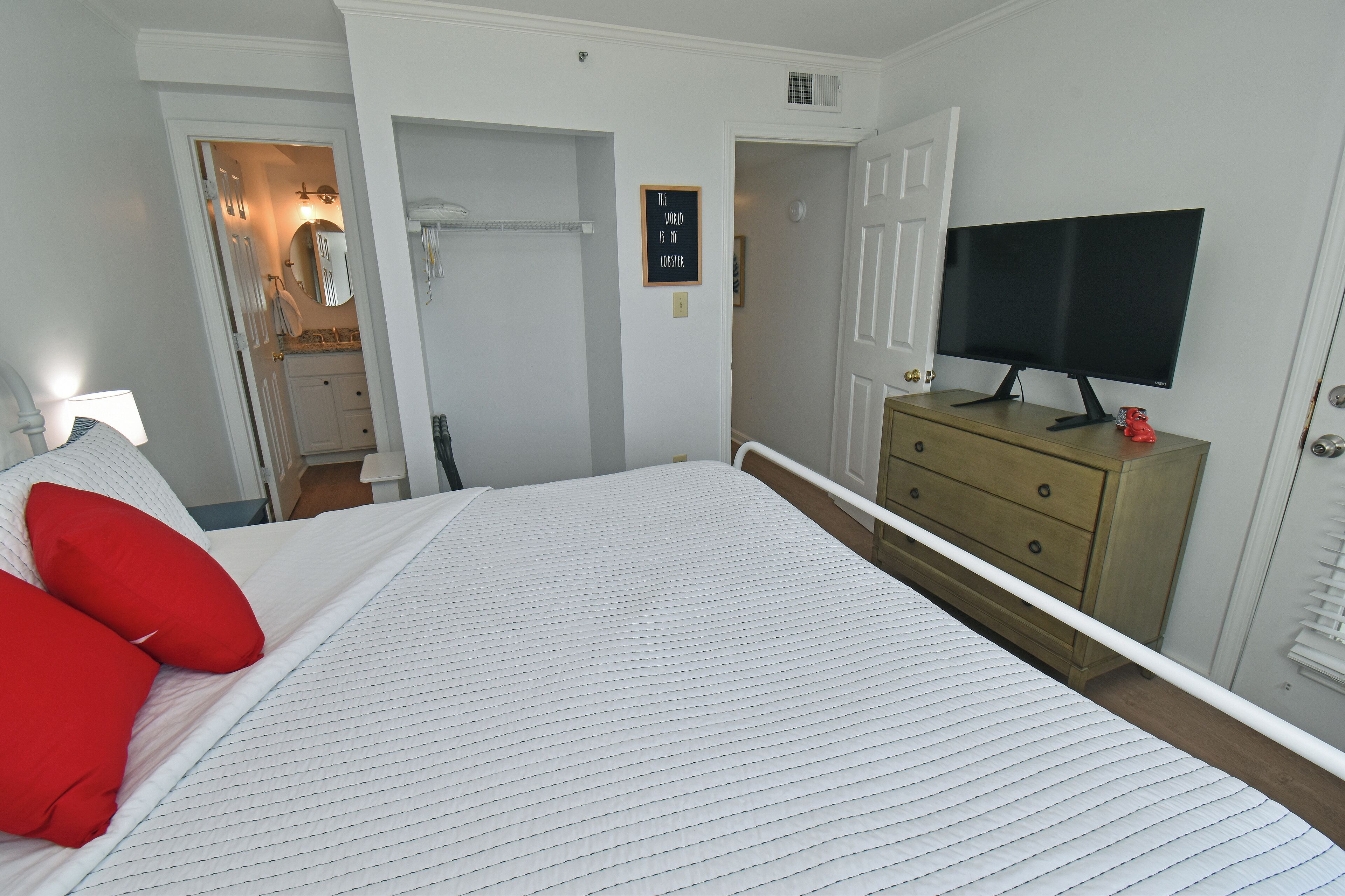 A bedroom with a bed, a dresser, a television, and a door leading to a bathroom.