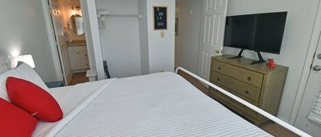 A bedroom with a bed, a dresser, a television, and a door leading to a bathroom.