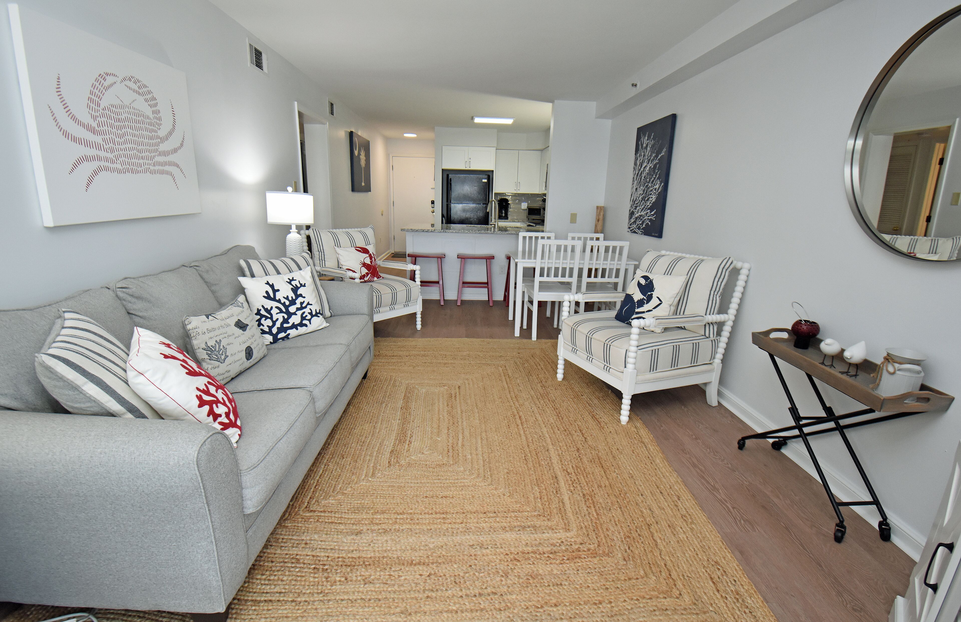 A modern living room with a grey sofa, striped armchairs, a small kitchen area, and a dining set.