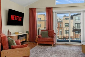 Ein modernes Wohnzimmer mit Kamin, einem roten Sessel, einer Couch und einem großen Fenster mit Vorhängen.