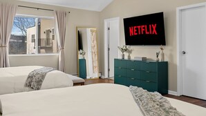 Makuuhuoneessa on kaksi sänkyä, televisio, jossa näkyy Netflix, lipasto ja ikkuna, jossa on verhot.