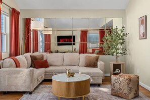 Ein Wohnzimmer mit einem Ecksofa, einem runden Couchtisch, einem Beistelltisch und einer Topfpflanze.