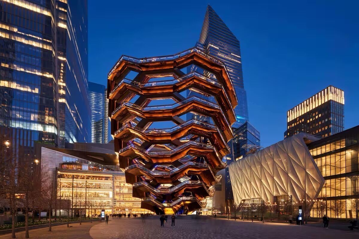 A modern architectural building with a unique honeycomb structure, surrounded by other contemporary buildings.