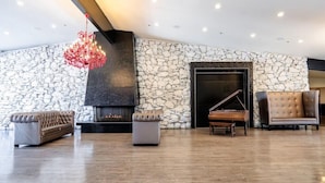 A spacious lobby with a stone wall, a fireplace, a grand piano, and modern seating.