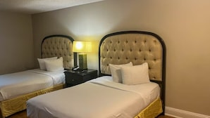 A hotel room with two beds, each with a tufted headboard and white bedding. There is a nightstand with a lamp between the beds.