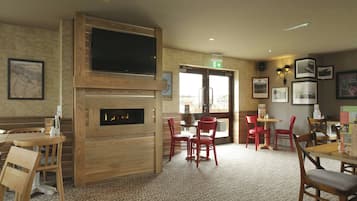 A restaurant with wooden walls, a fireplace, red chairs, and a television.