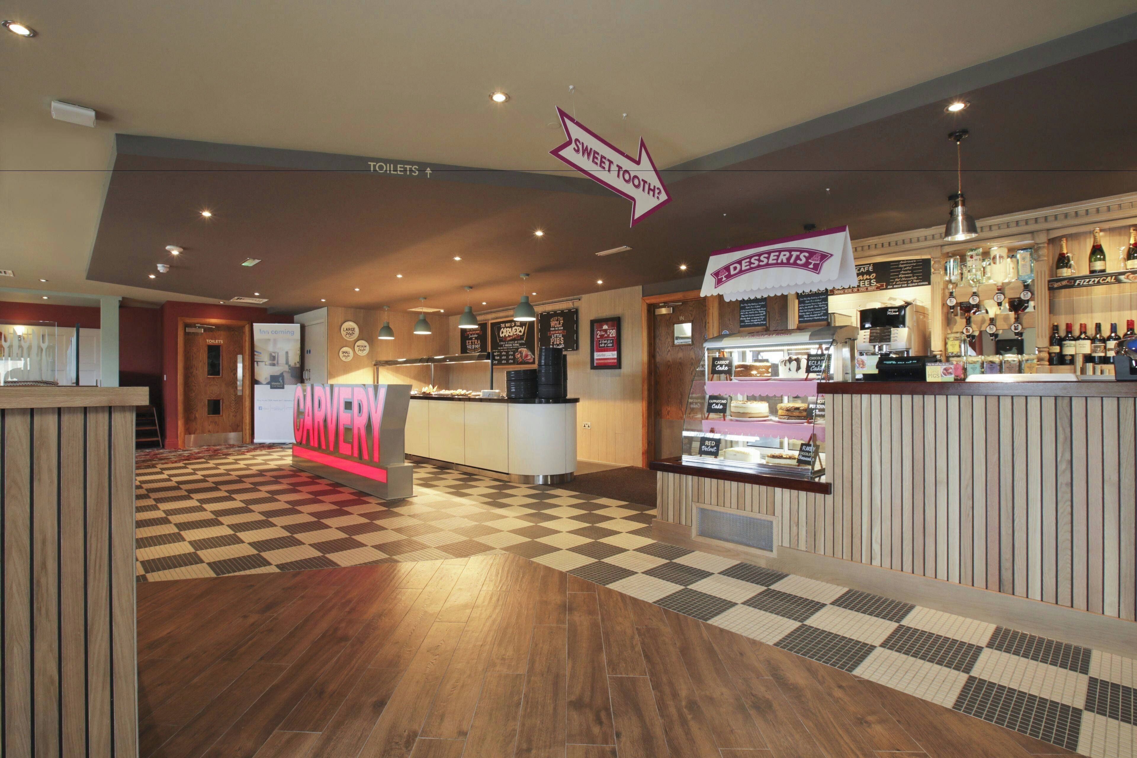 A restaurant interior with a checkered floor, a counter with desserts, and a sign pointing to the toilets.
