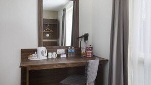 Ett hotellrum med ett skrivbord i trä, en spegel, en hårtork, en vattenkokare, en kopp, en tallrik med bakverk och en meny.
