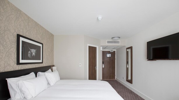 Ett hotellrum med en stor säng, en TV som hänger på väggen och en inramad tavla på väggen.