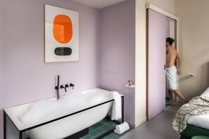 Un baño moderno con bañera, una obra de arte enmarco y una puerta visible que da a otra habitación.