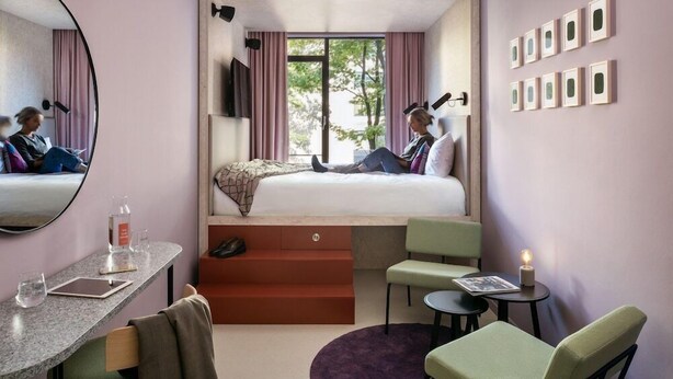 Une chambre d’hôtel de taille réduite, comprenant un lit, un bureau, une chaise et une petite table.