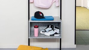 Une pièce bien rangée, avec un portant sur lequel sont suspendus un t-shirt rose, une casquette noire et une paire de baskets. Un sac jaune est posé sur le sol.