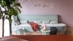 Un salon moderne avec un canapé bleu clair, une petite table ronde, un vase rose et un plaid rouge.