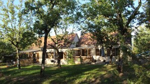 Una casa rústica con porche, rodeada de árboles y un jardín cubierto de césped.