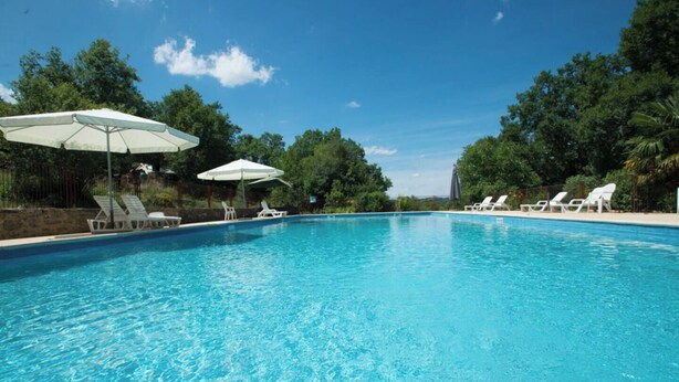 Piscina azul cristalina con sillas de descanso blancas y sombrillas, rodeada de árboles.