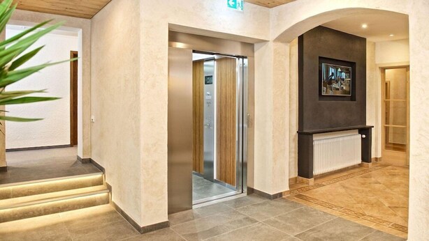 A hotel lobby with a staircase, elevator, and a framed artwork on the wall. - Interest of Bavaria (Oberstaufen)
