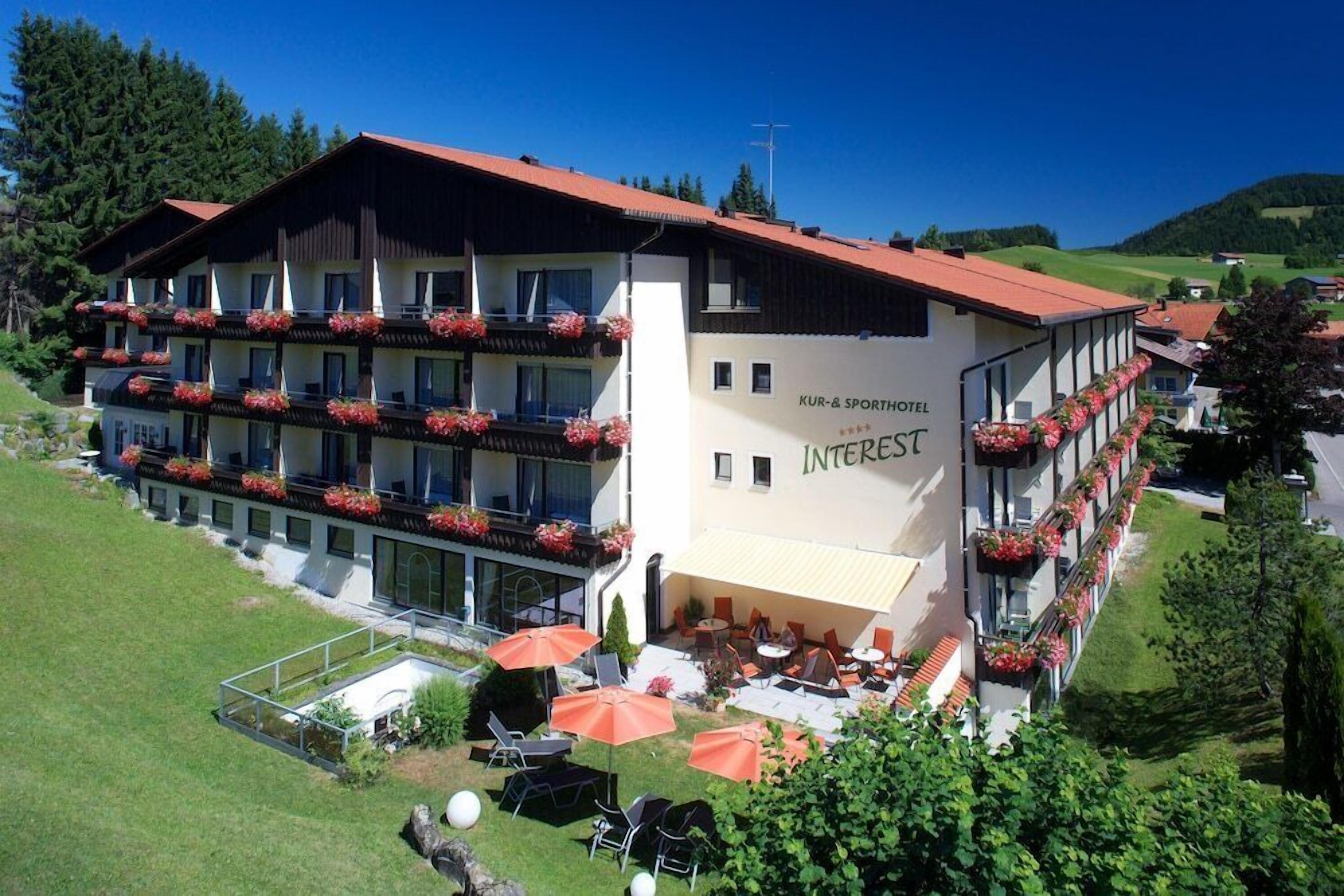 Ein mehrstöckiges Hotel mit Balkonen, die mit Blumen geschmückt sind, Sitzgelegenheiten im Freien und freiem Blick auf die umliegende Landschaft.